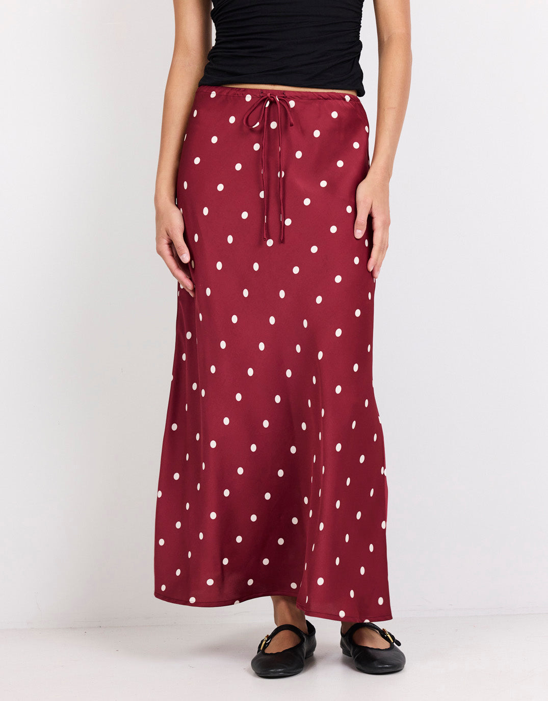 Image of a model wearing Skirts. Product name - Rarity Satin Tie Waist Bias Maxi Skirt Wine/Cream Polka Dot in Wine/Cream Polka Dot colour by brand - Stories Be Told