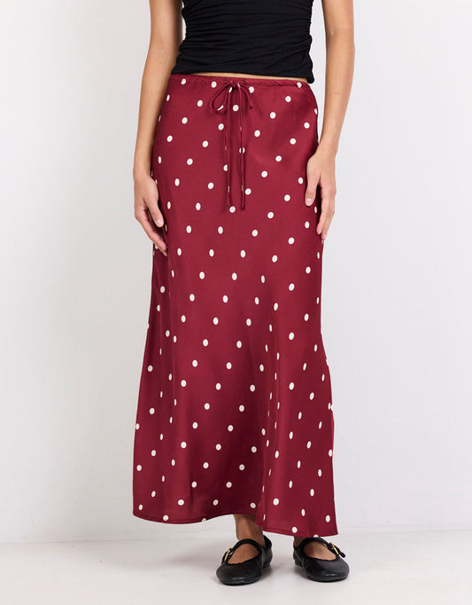 Image of a model wearing Skirts. Product name - Rarity Satin Tie Waist Bias Maxi Skirt Wine/Cream Polka Dot in Wine/Cream Polka Dot colour by brand - Stories Be Told
