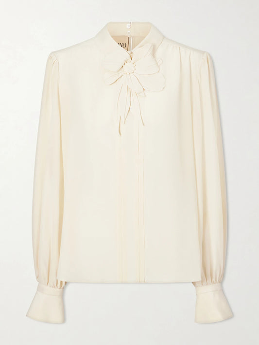 Image of a model wearing Tops. Product name - Bow-embellished Silk-crepe De Chine Blouse in Cream colour by brand - Valentino Garavani