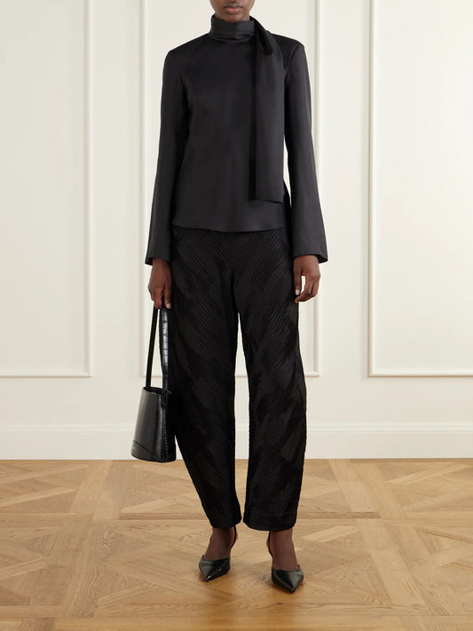 Image of a model wearing Pants. Product name - Plissé Satin Tapered Pants in Black colour by brand - RÓHE