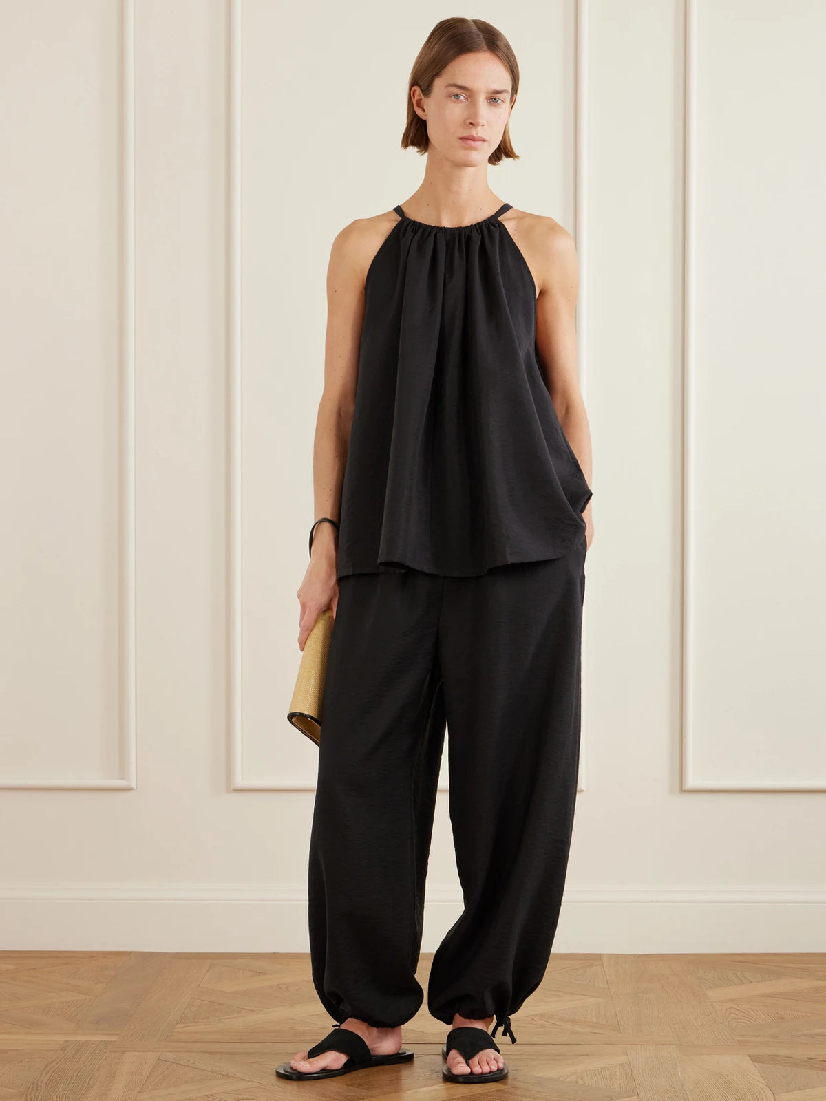 Image of a model wearing Tops. Product name - Gathered Lyocell-blend Halterneck Top in Black colour by brand - TOTEME