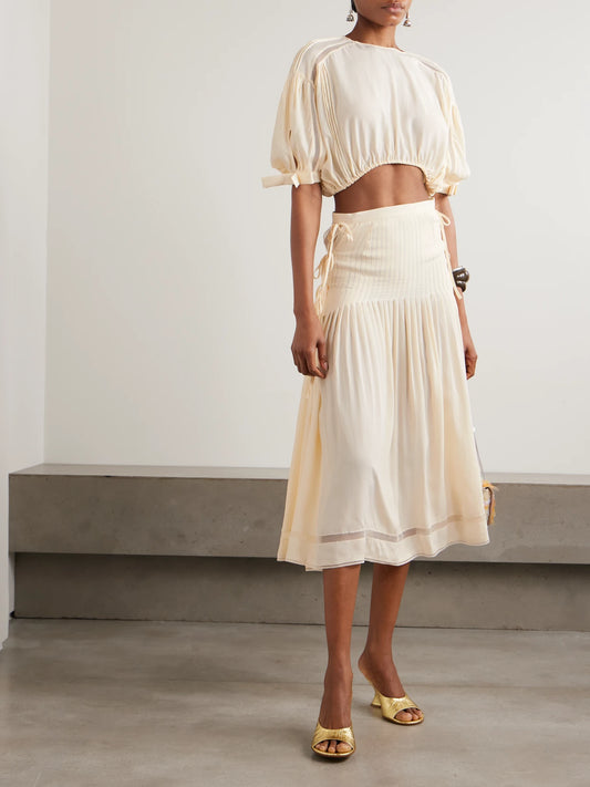 Image of a model wearing Tops. Product name - Cropped Bow-detailed Lace-trimmed Pleated Crepe Top in Ecru colour by brand - RABANNE
