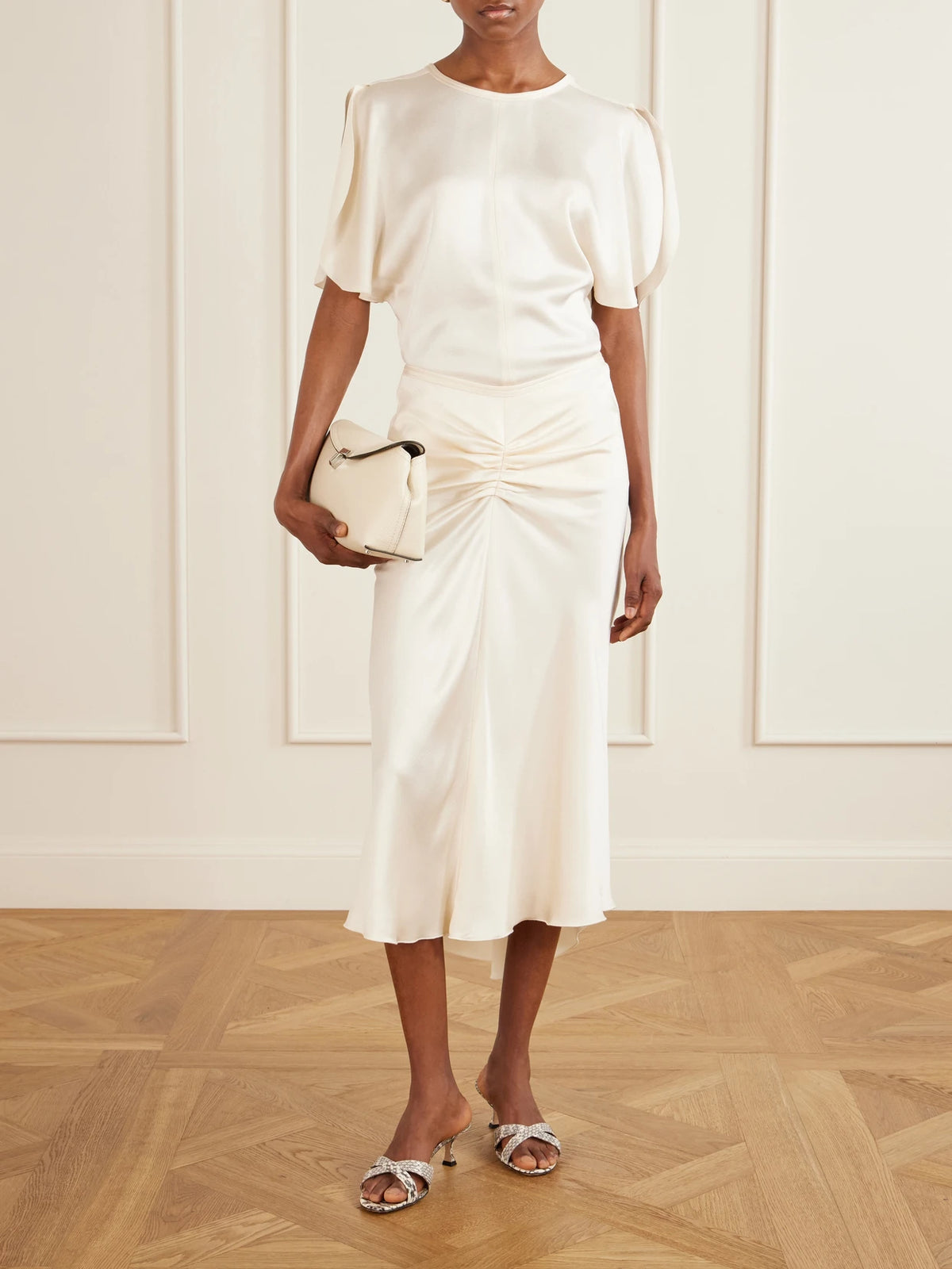 Image of a model wearing Skirts. Product name - Bela Ruched Satin Midi Skirt in Off-white colour by brand - Victoria Beckham