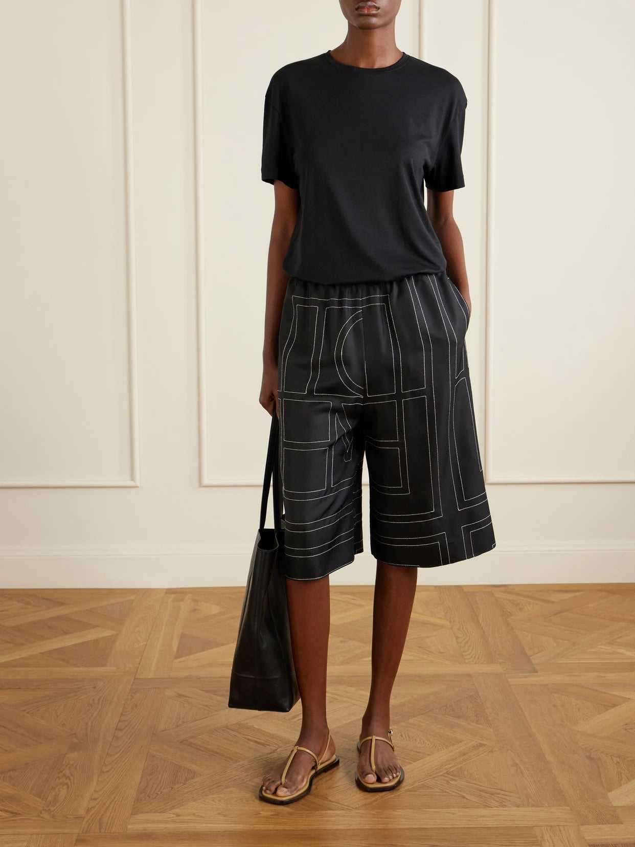 Image of a model wearing Shorts. Product name - Embroidered Silk Shorts in Black colour by brand - TOTEME