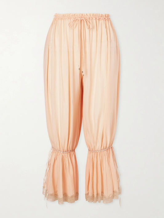 Image of a model wearing Pants. Product name - Ruffled Pleated Lace-trimmed Silk-charmeuse Balloon Pants in Peach colour by brand - Chloé