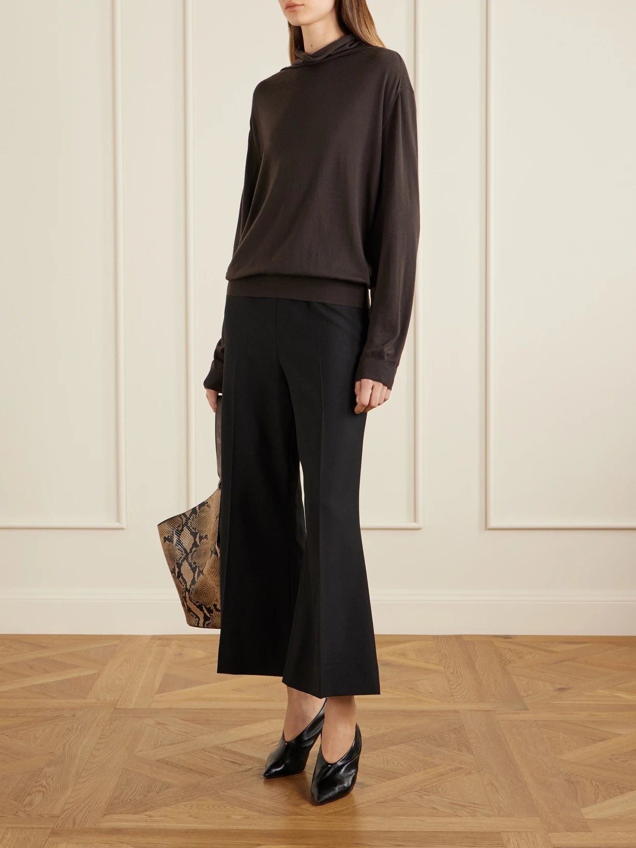 Image of a model wearing Pants. Product name - Walter Wool Mid-rise Flared Leg Pants in Black colour by brand - KHAITE