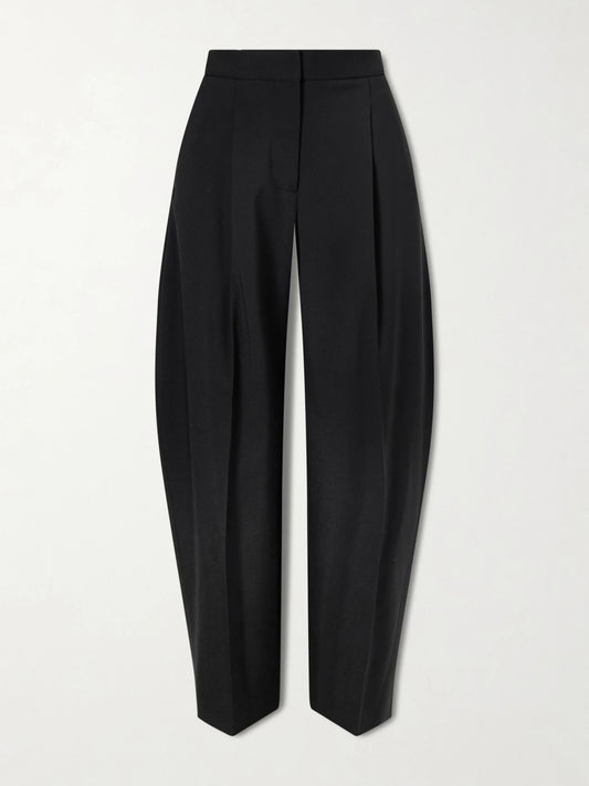 Image of a model wearing Pants. Product name - Pleated Wool-blend Gabardine Tapered Pants in Black colour by brand - Alaïa