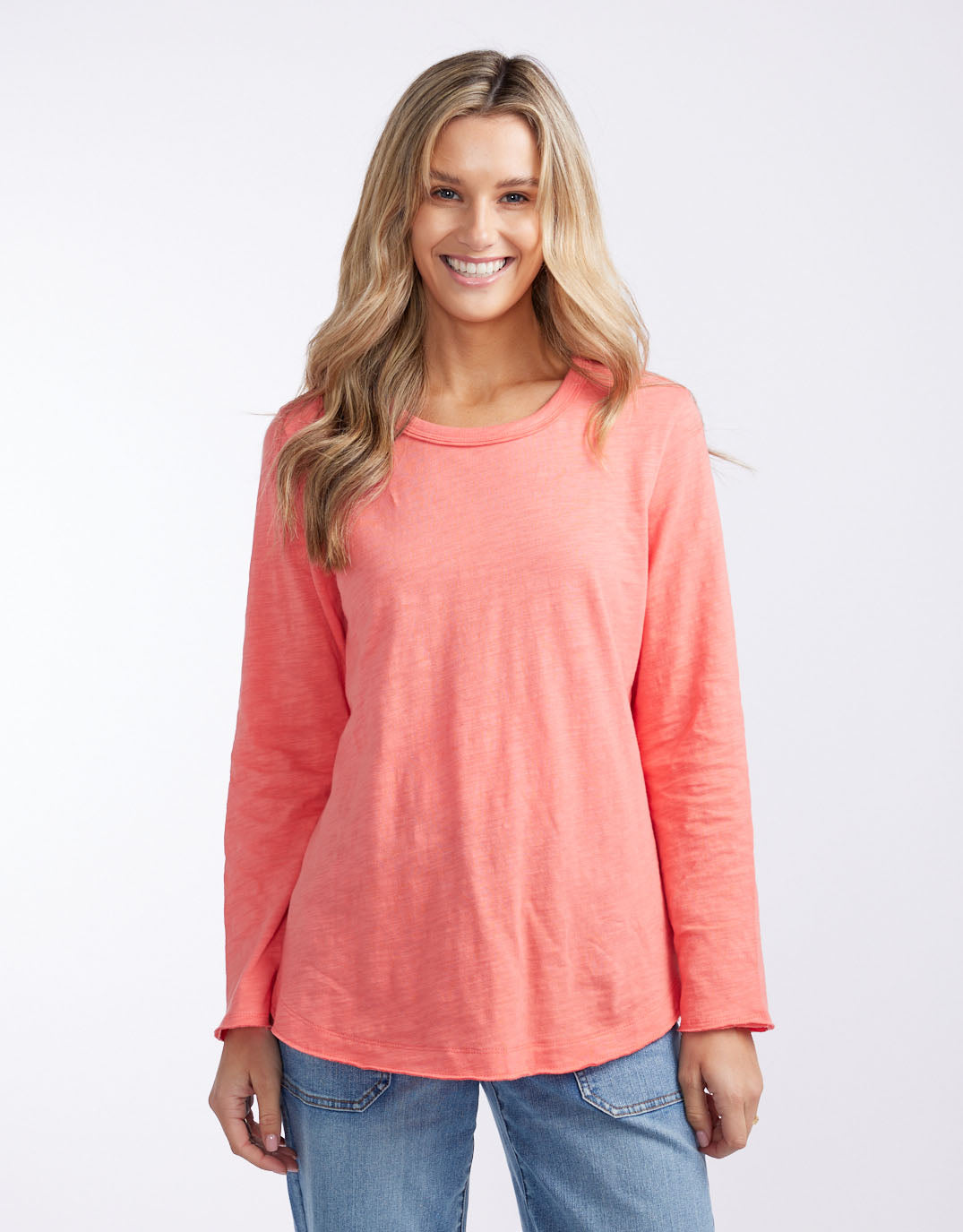 Image of a model wearing Tops. Productname: Essential Scoop Hem Long Sleeve T-Shirt - in Melon colour by brand - White & Co.