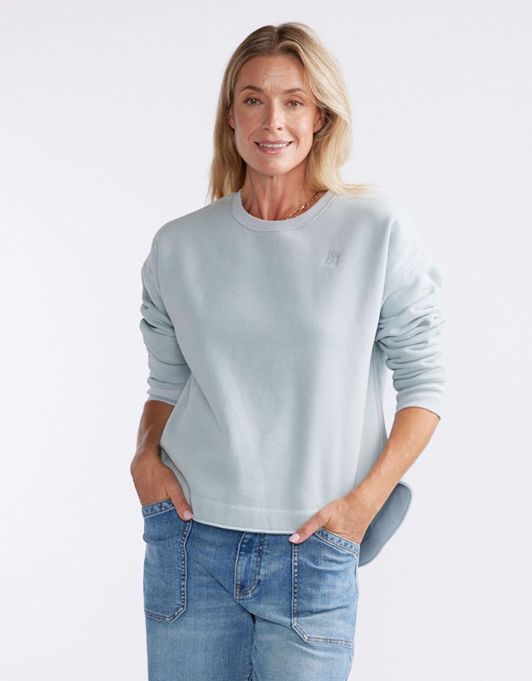 Image of a model wearing Tops. Productname: Monogram Fleece Scoop Hem Sweat - in Light Blue colour by brand - White & Co.